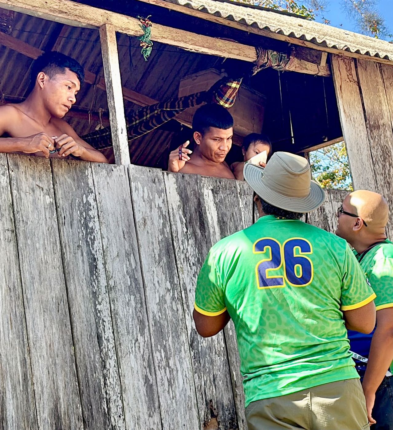 A team member talking with a family through the window of a wooden house in Brazil